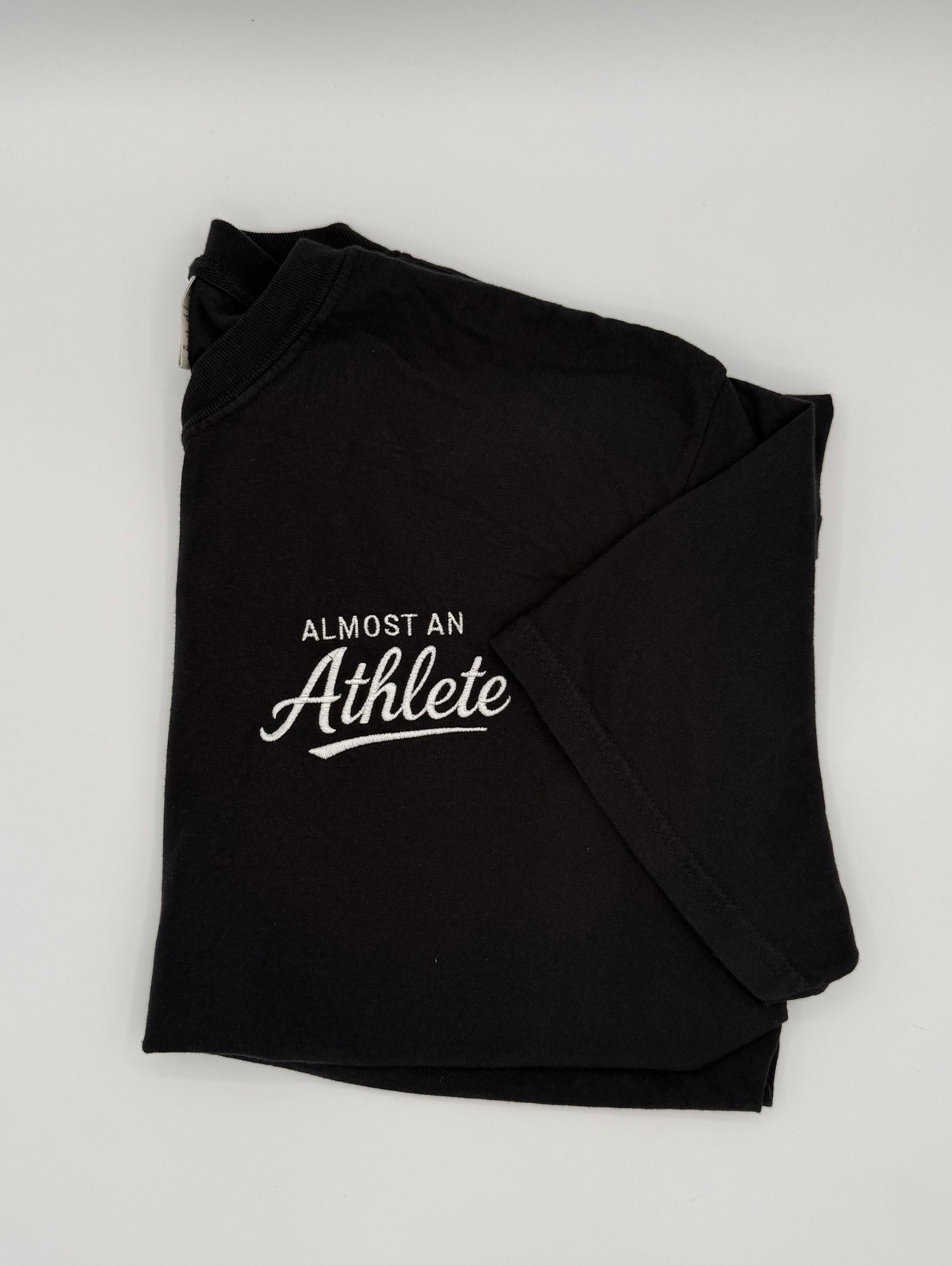Black t-shirt with 'Almost an Athlete' text embroidered in white on the right top chest.