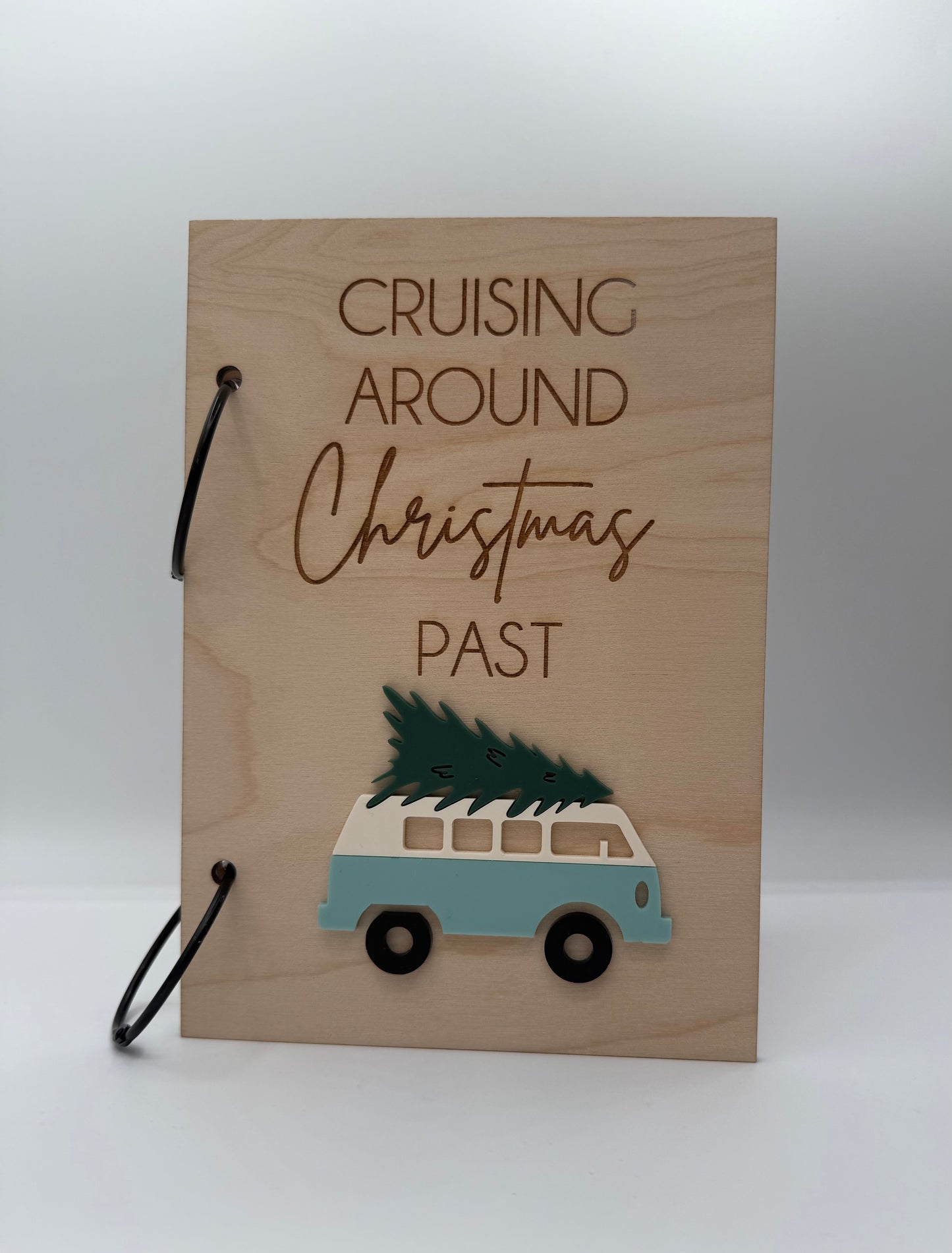 Wooden Christmas greeting card keeper with an acrylic light blue retro van carrying a christmas tree design. The words 'Cruising Around Christmas Past' is laser engraved on the top with black binder rings.
