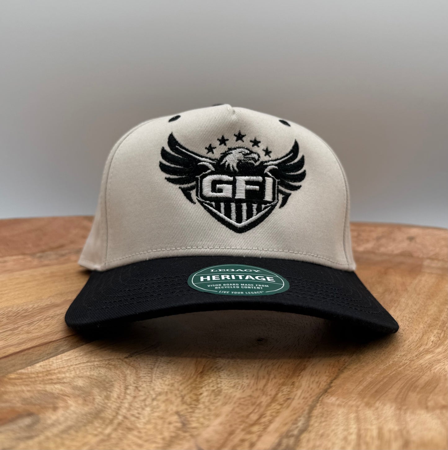 Beige and black hat with GFI logo that includes an eagle on a wooden surface