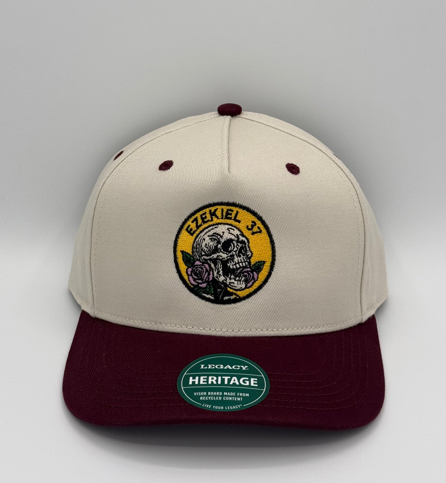 Beige and maroon two toned hat with a skill holding a rose design embroidered in a circle with the words Ezekiel 37