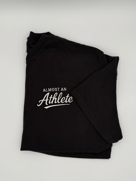 Black t-shirt with 'Almost an Athlete' text embroidered in white  on the right top chest.