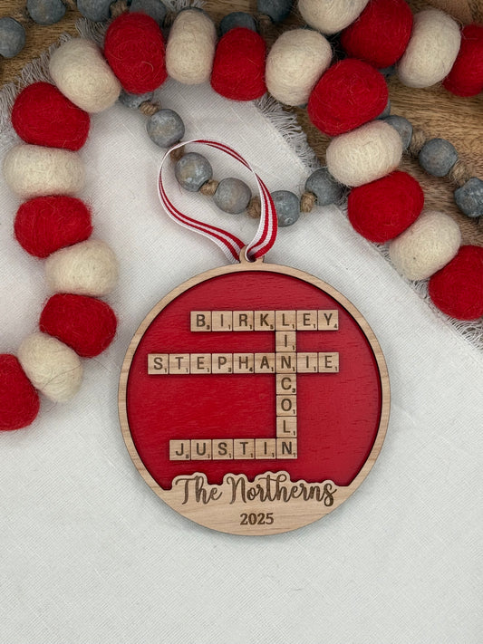 Decorative wooden circle ornament with personalized names laser engraved in a crossword pattern on red background. 