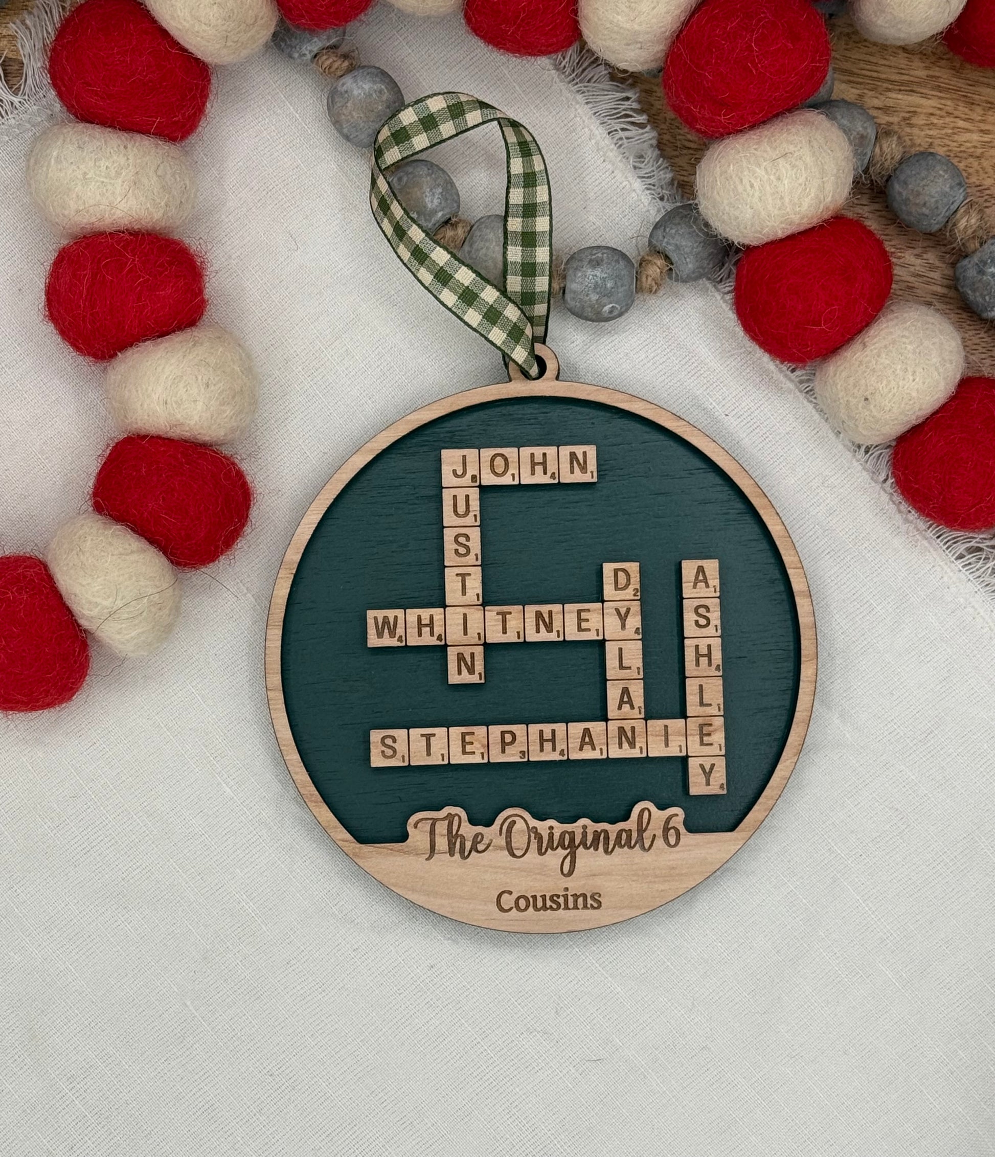 Decorative wooden circle ornament with personalized names laser engraved in a crossword pattern on dark green background. 