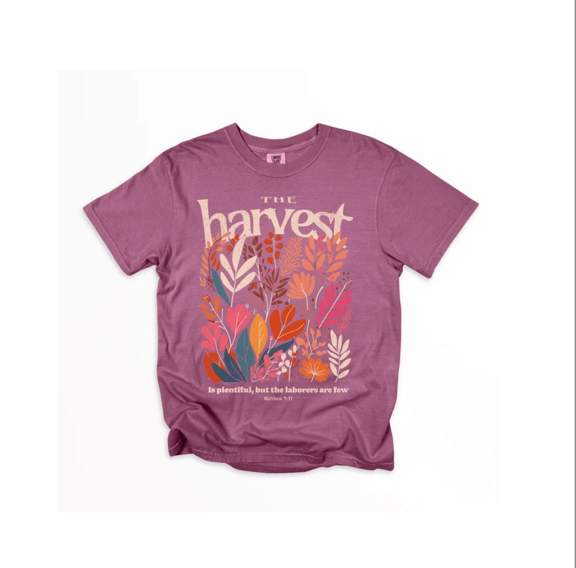 A heathered purple t-shirt with a colorful graphic print featuring the word 'harvest' in a stylized font above an illustration of autumn leaves, with a Bible verse printed below, shown flat on a white background.