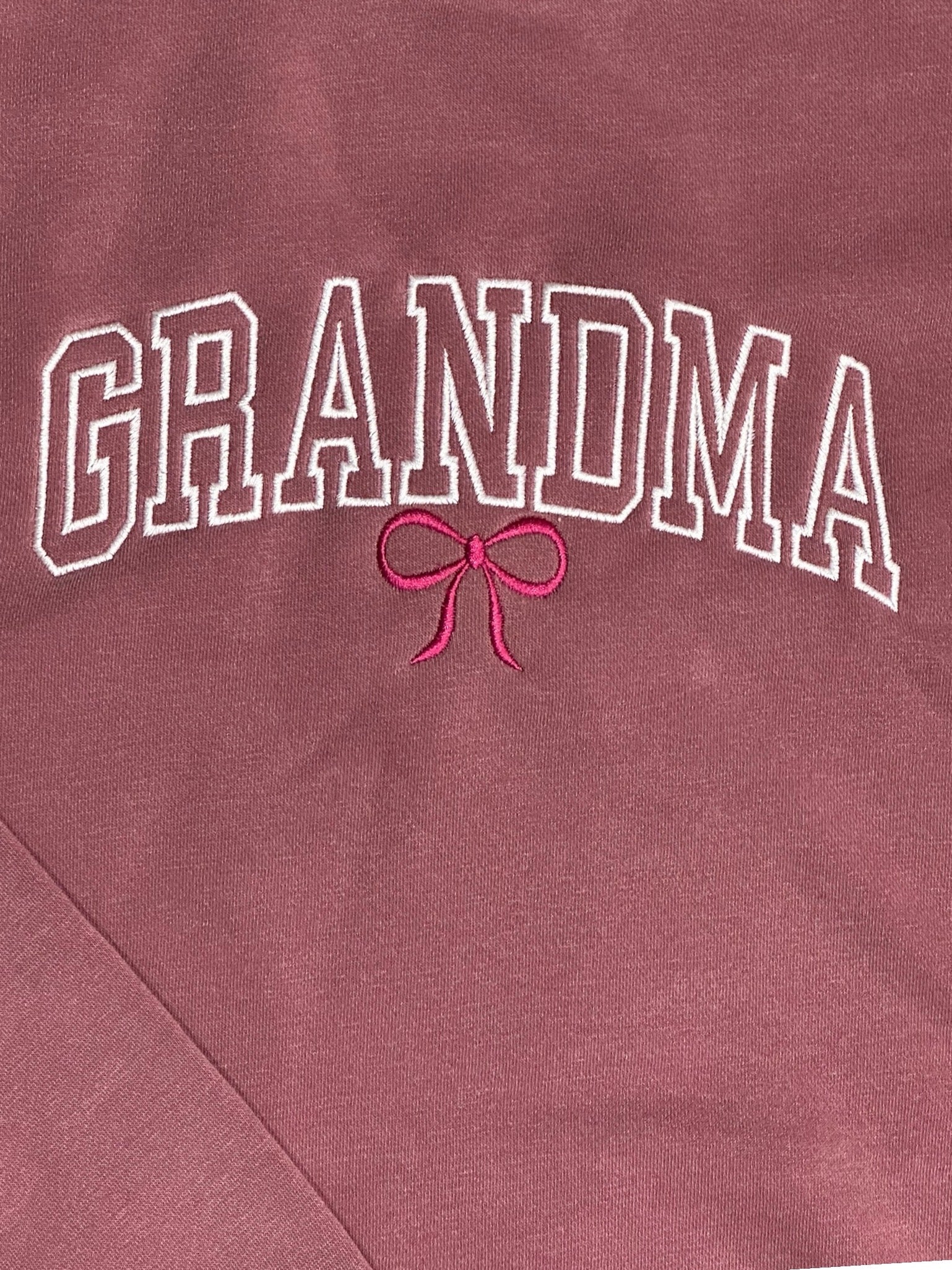 Maroon sweatshirt with the text 'Grandma' embroidered in a white varsity outline font. This design features a maroon embroidered bow underneath.