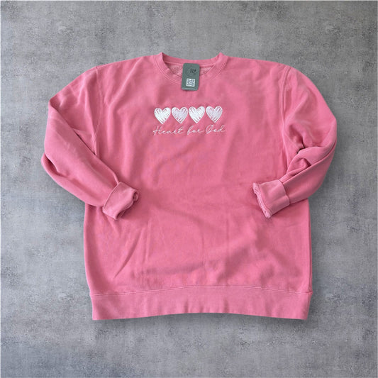 Pink sweatshirt with heart designs and text that says Heart for God on a grey surface full front view