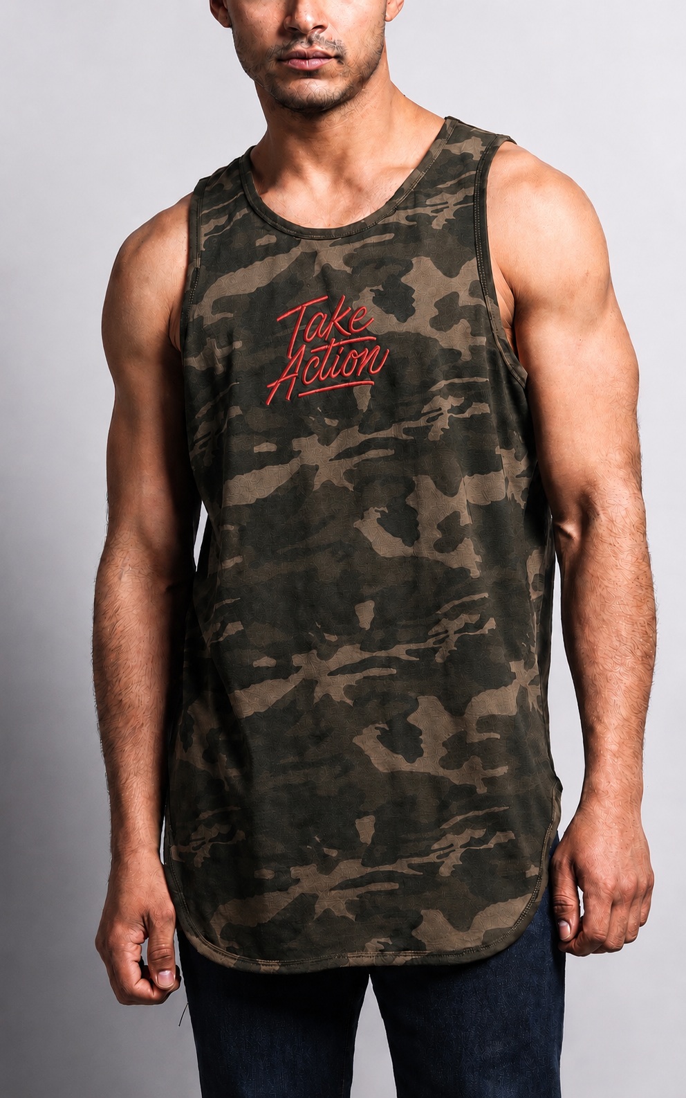 A man wearing a sleeveless camouflage tank top with red 'Take Action' text on the chest, paired with dark blue jeans, against a light gray studio background.