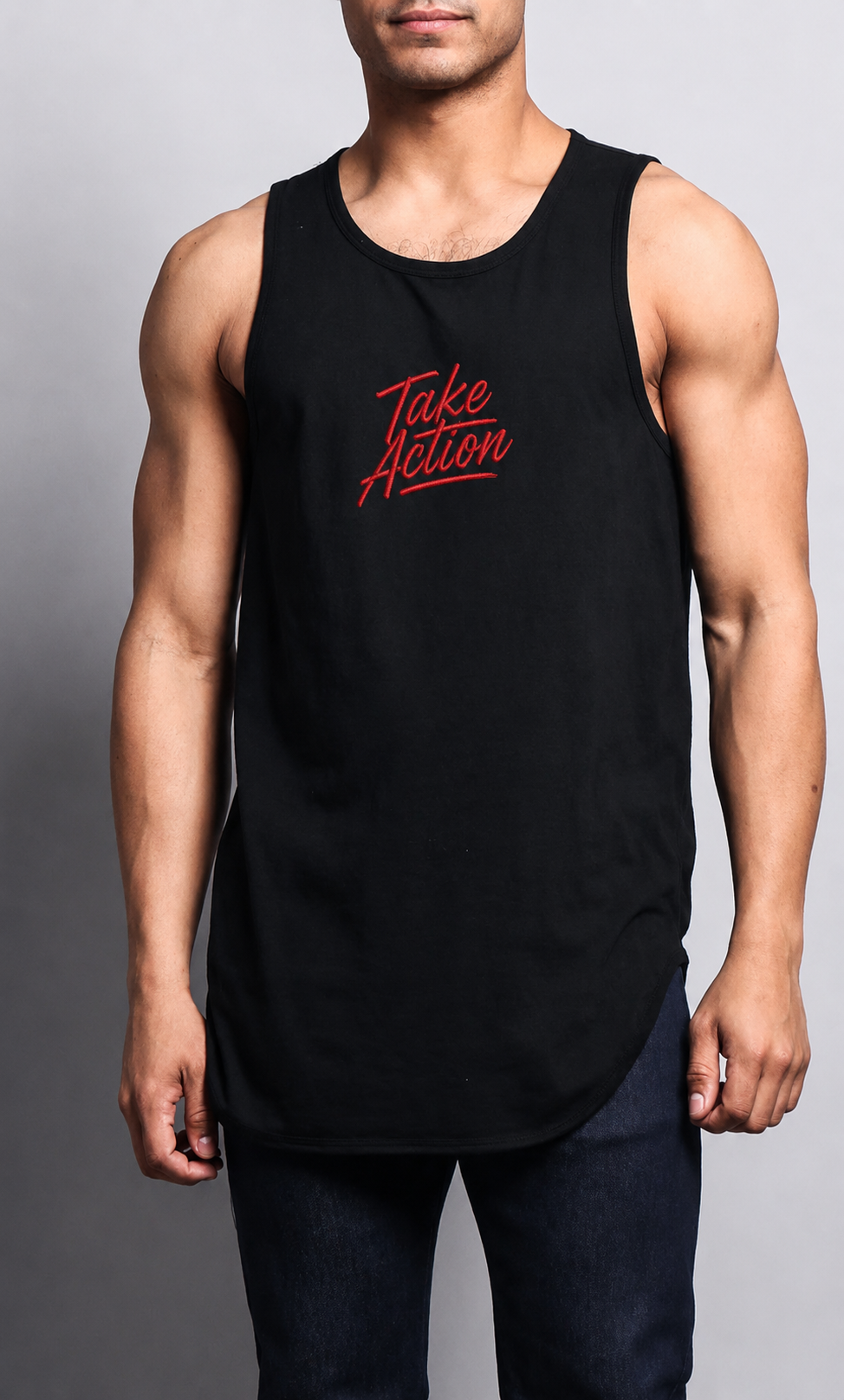 A muscular man wearing a black sleeveless tank top with 'Take Action' printed in red script on the chest, paired with dark jeans, against a neutral gray studio background.