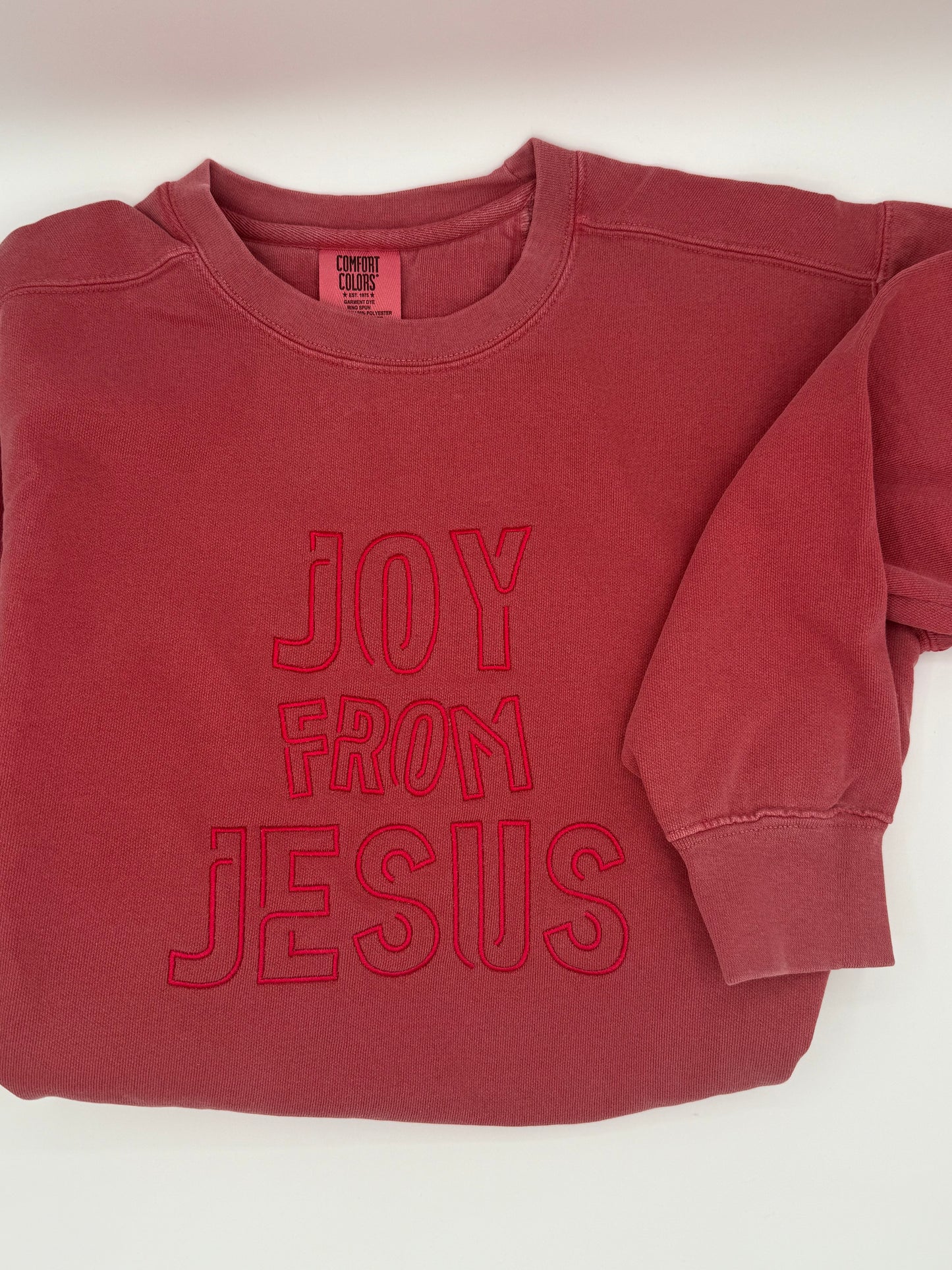 Red sweatshirt with the words 'Joy from Jesus' embroidered in a tone on tone red.