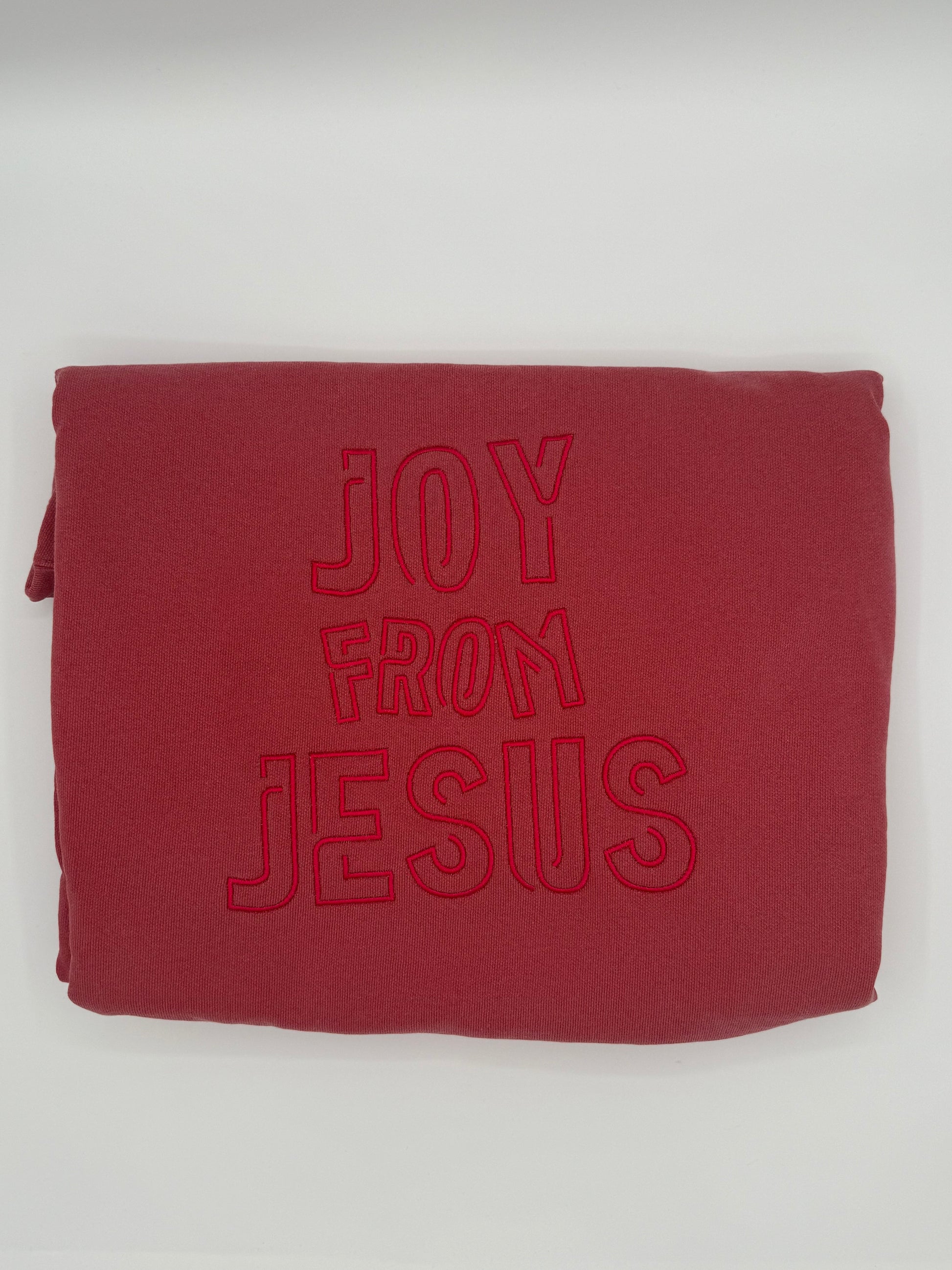 Red sweatshirt with the words 'Joy from Jesus' embroidered in a tone on tone red. This is a folded up display view.