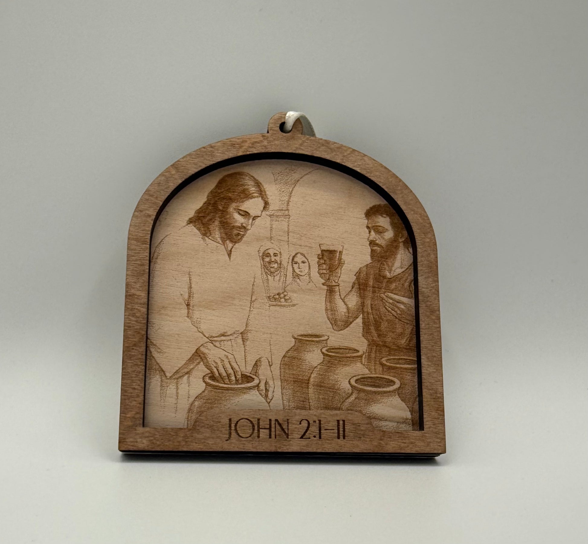 Wooden ornament with a laser engraved scene depicting Jesus turining water into wine. Bible verses John 2:1-11.