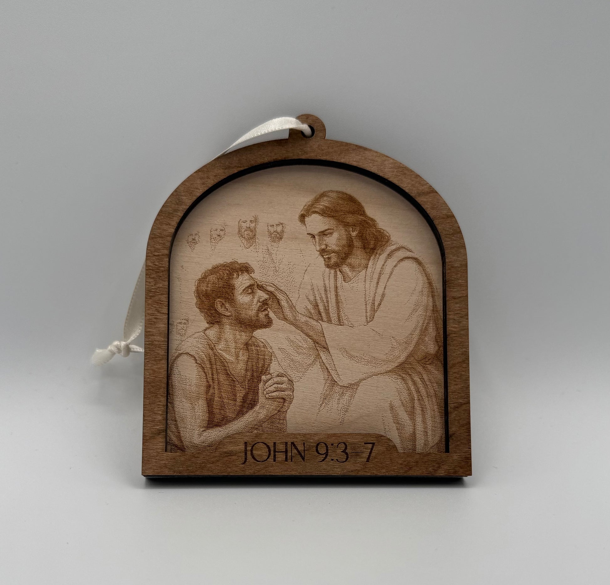 Wooden ornament with a laser engraved scene depicting Jesus healing a man. Bible verses John 9:3-7.