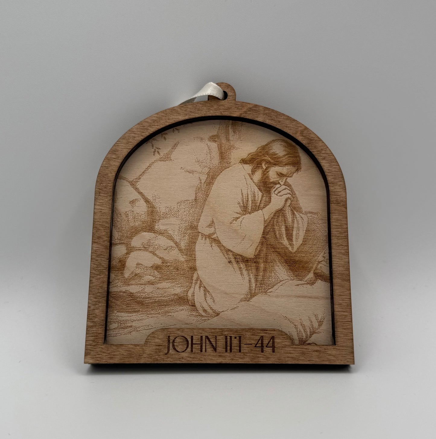 Wooden ornament with a laser engraved scene depicting Jesus praying on his knees. Bible verses John 11:1-44.
