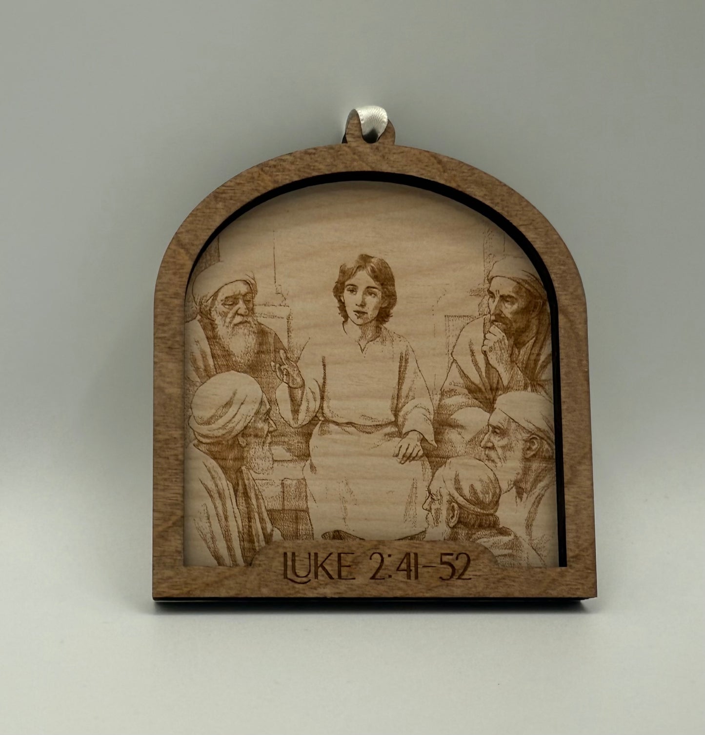 Wooden ornament with a laser engraved scene depicting a young Jesus talking to 5 men. Bible verses Luke 2:41-52.