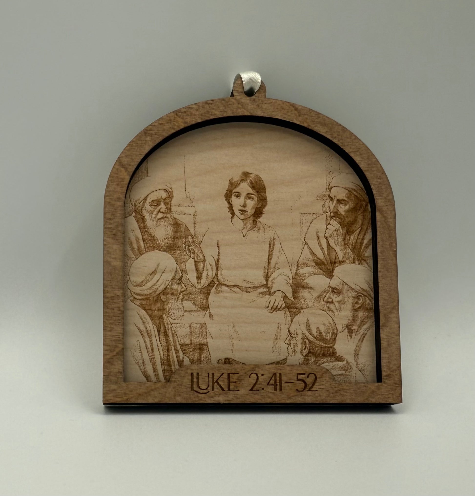 Wooden ornament with a laser engraved scene depicting a young Jesus talking to 5 men. Bible verses Luke 2:41-52.