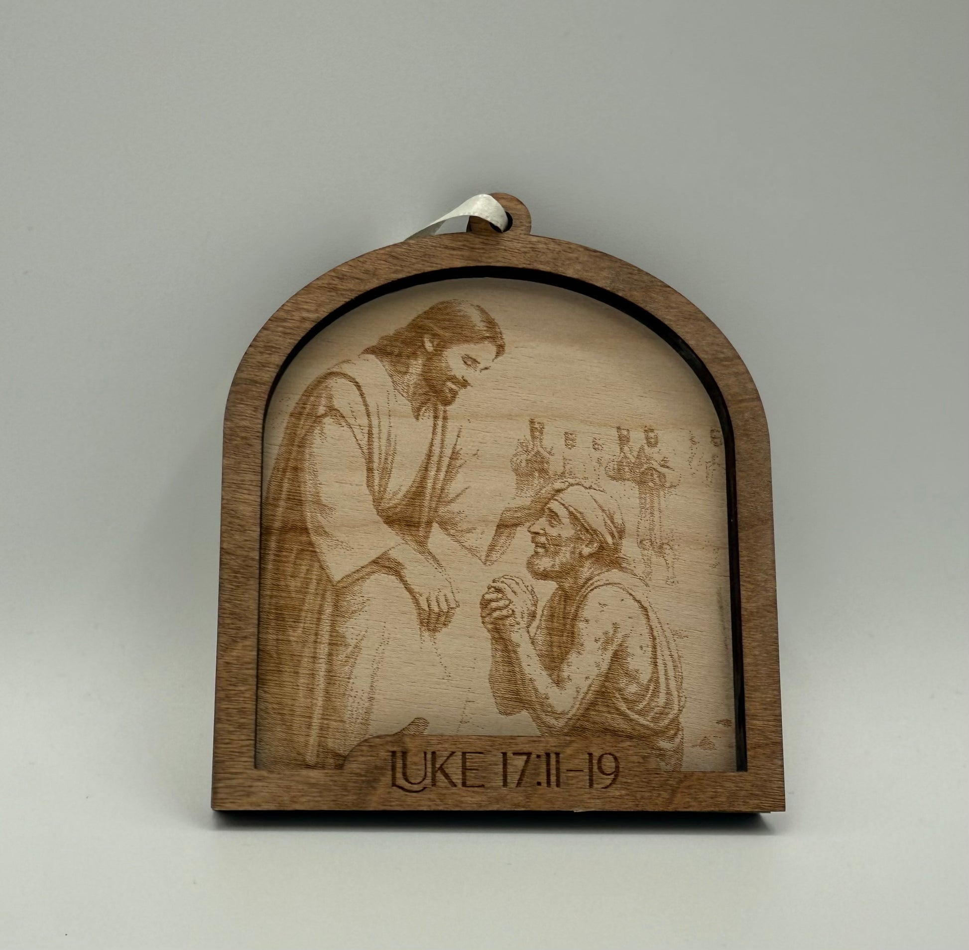 Wooden ornament with a laser engraved scene depicting Jesus laying hands on a man. Bible verses Luke 17:11-19.