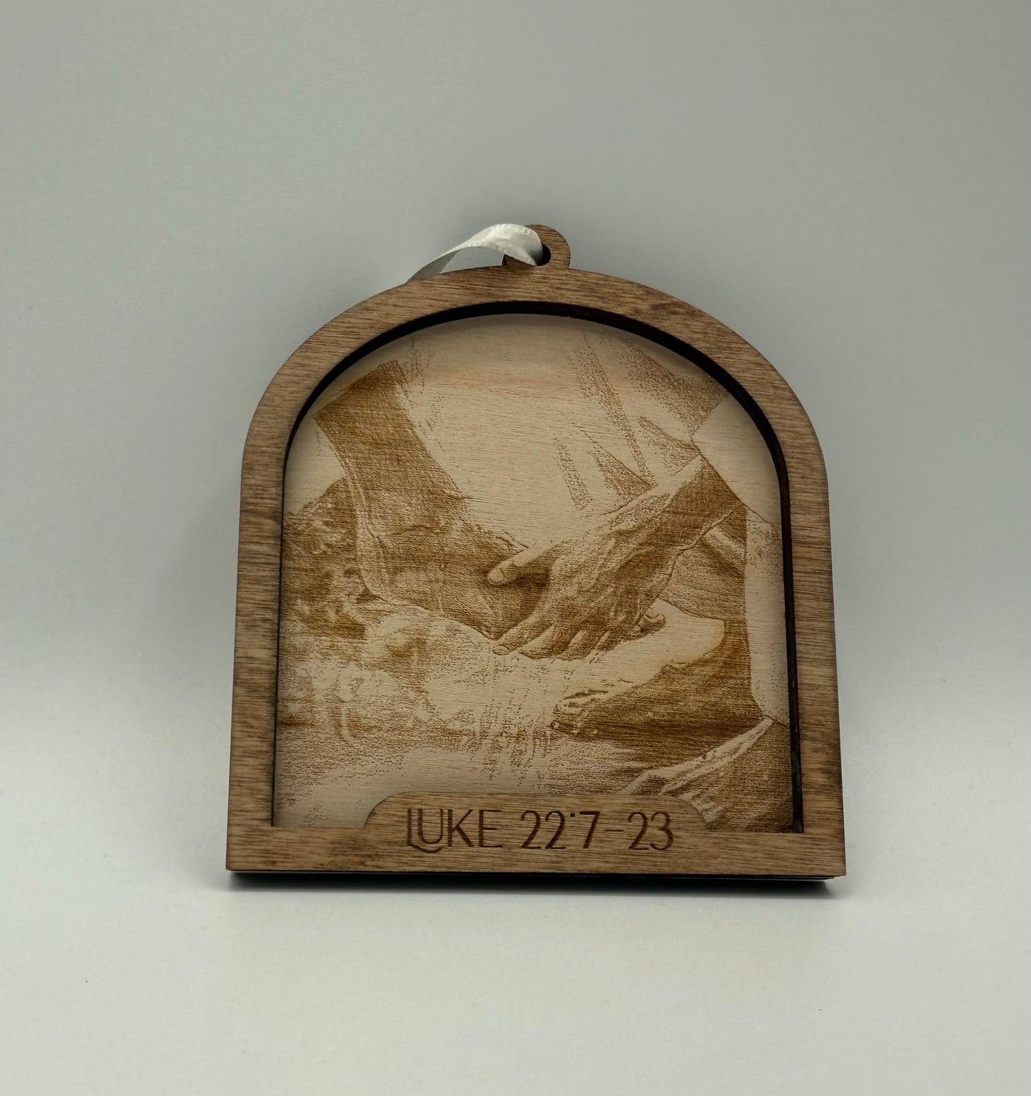 Wooden ornament with a laser engraved scene depicting Jesus' feet being washed. Bible verses Luke 22:7-23