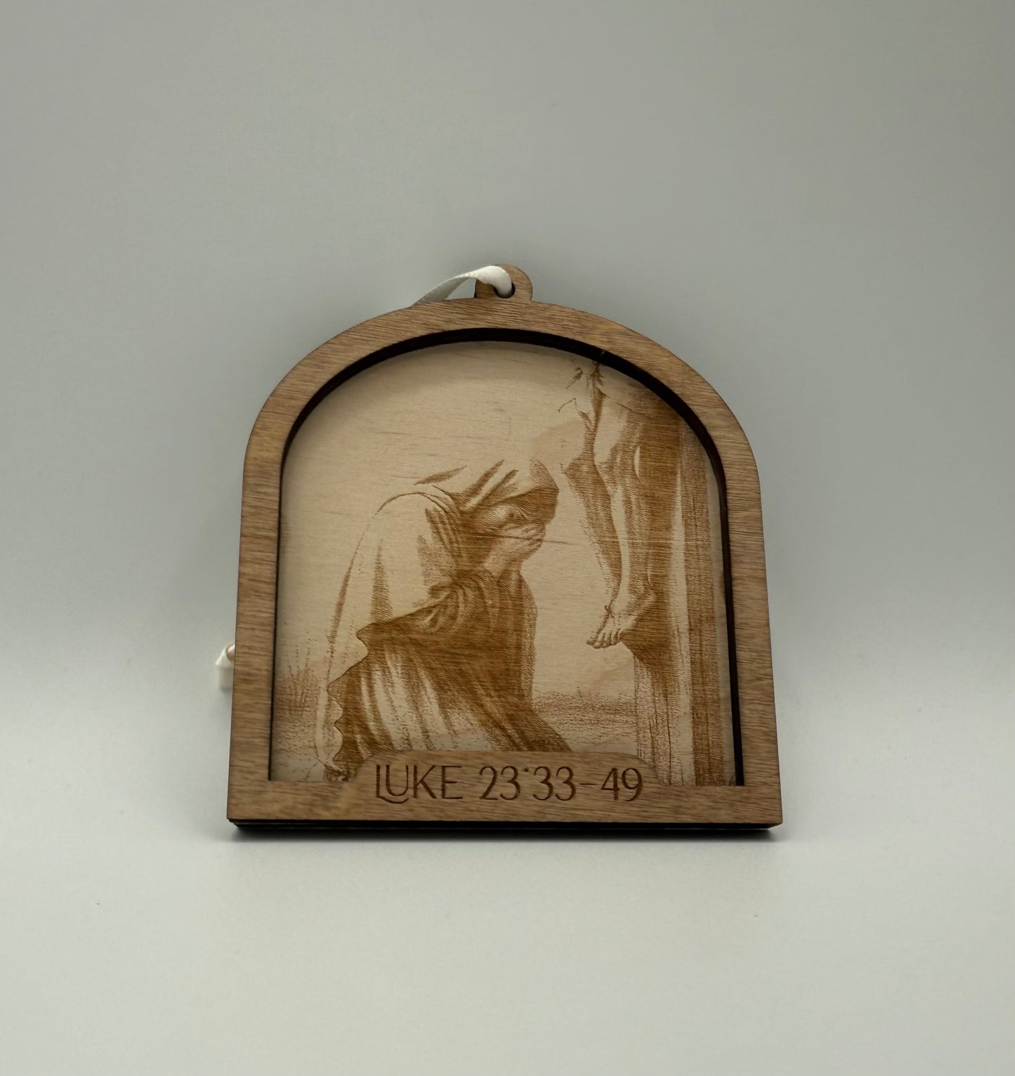 Wooden ornament with a laser engraved scene depicting a woman on her knees praying. Bible verses Luke 23:33-49.