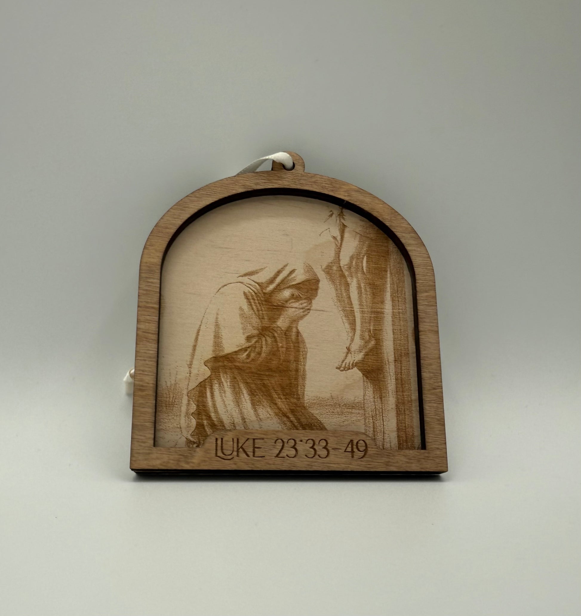 Wooden ornament with a laser engraved scene depicting a woman on her knees praying. Bible verses Luke 23:33-49.