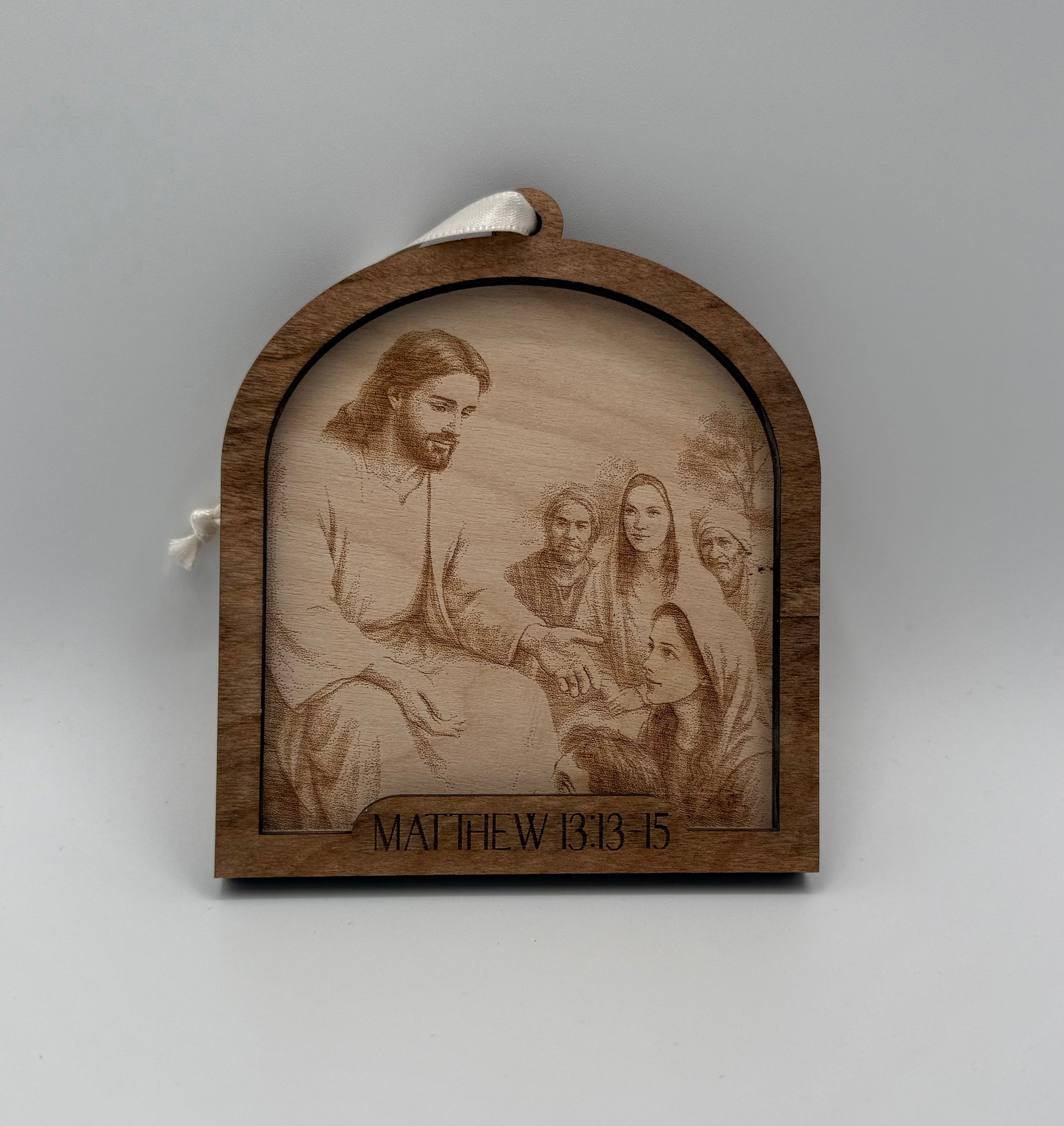 Wooden ornament with a laser engraved scene depicting Jesus praying talking to a young woman. Bible verses Matthew 13:13-15.