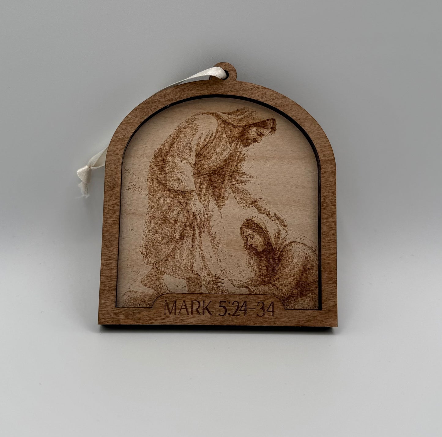 Wooden ornament with a laser engraved scene depicting a woman touching the hem of Jesus. Bible verses Mark 5:24-34.