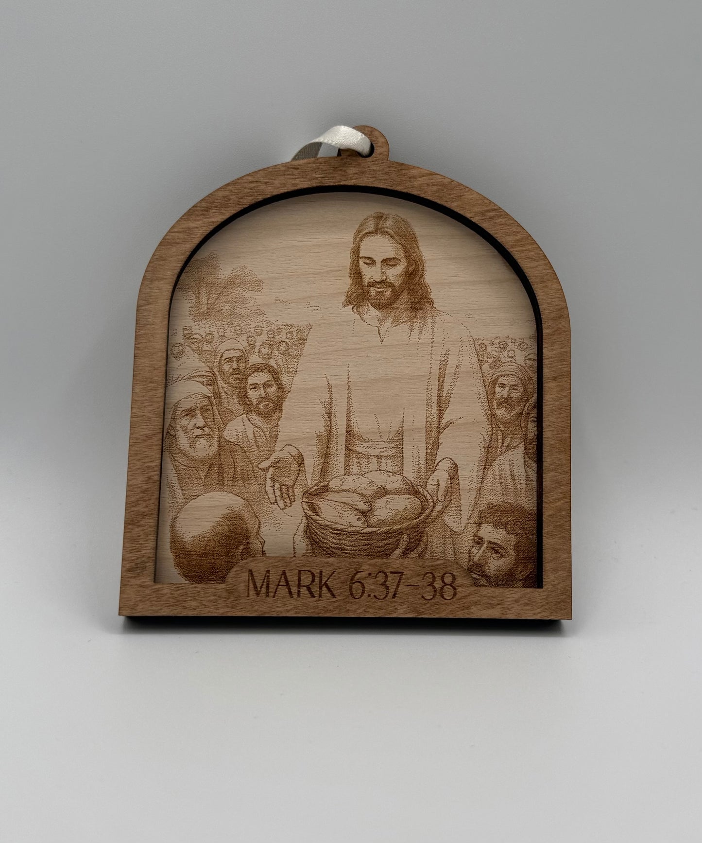 Wooden ornament with a laser engraved scene depicting Jesus feeding a crowd Bible verses Mark 6:37-38.