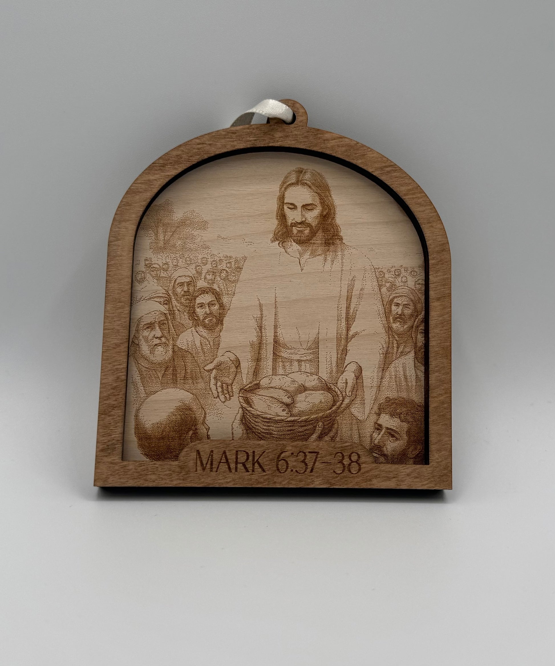 Wooden ornament with a laser engraved scene depicting Jesus feeding a crowd Bible verses Mark 6:37-38.