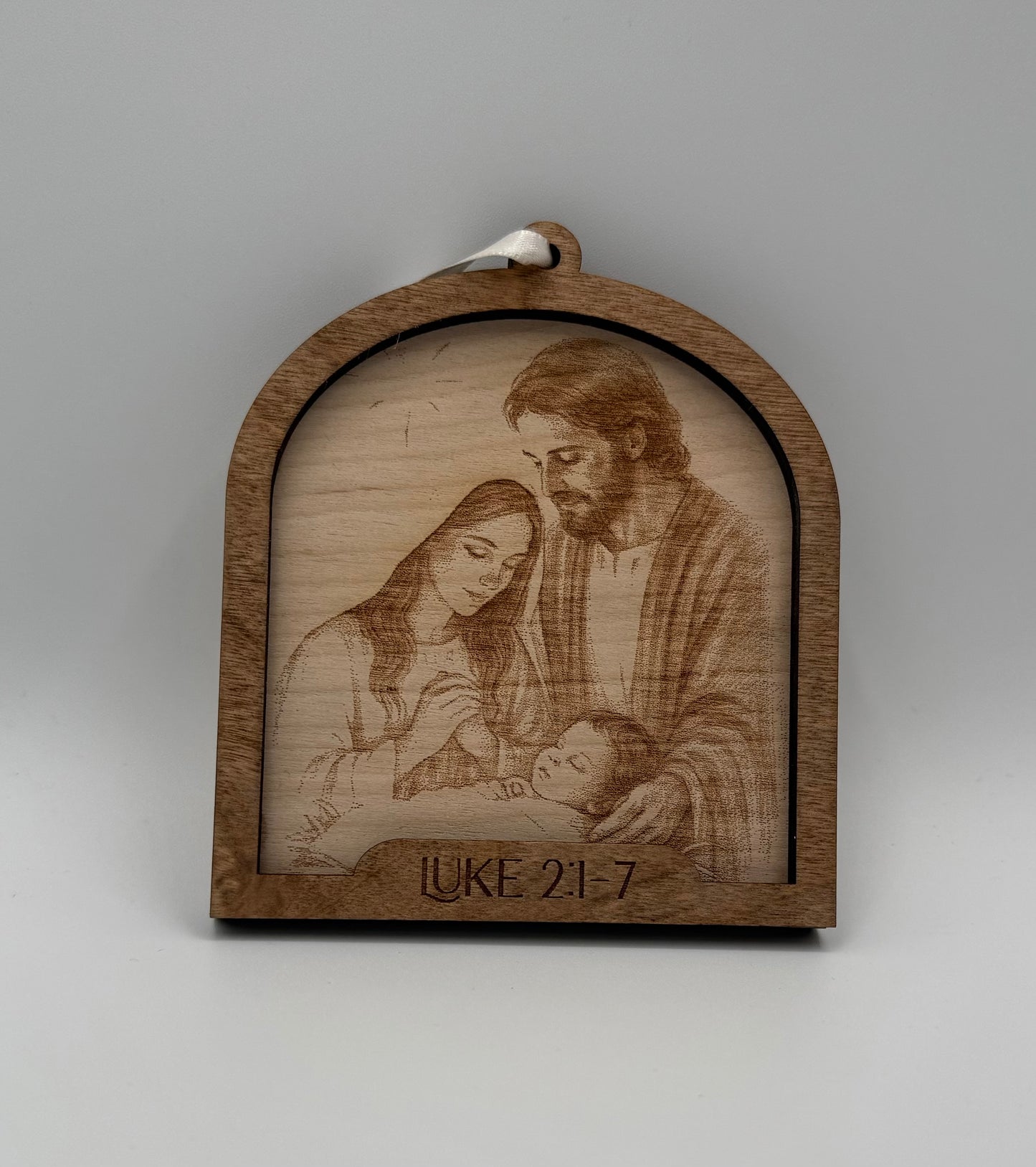 Wooden ornament with a laser engraved scene depicting Mary and Joseph looking at baby Jesus. Bible verses Luke2 2:1-7