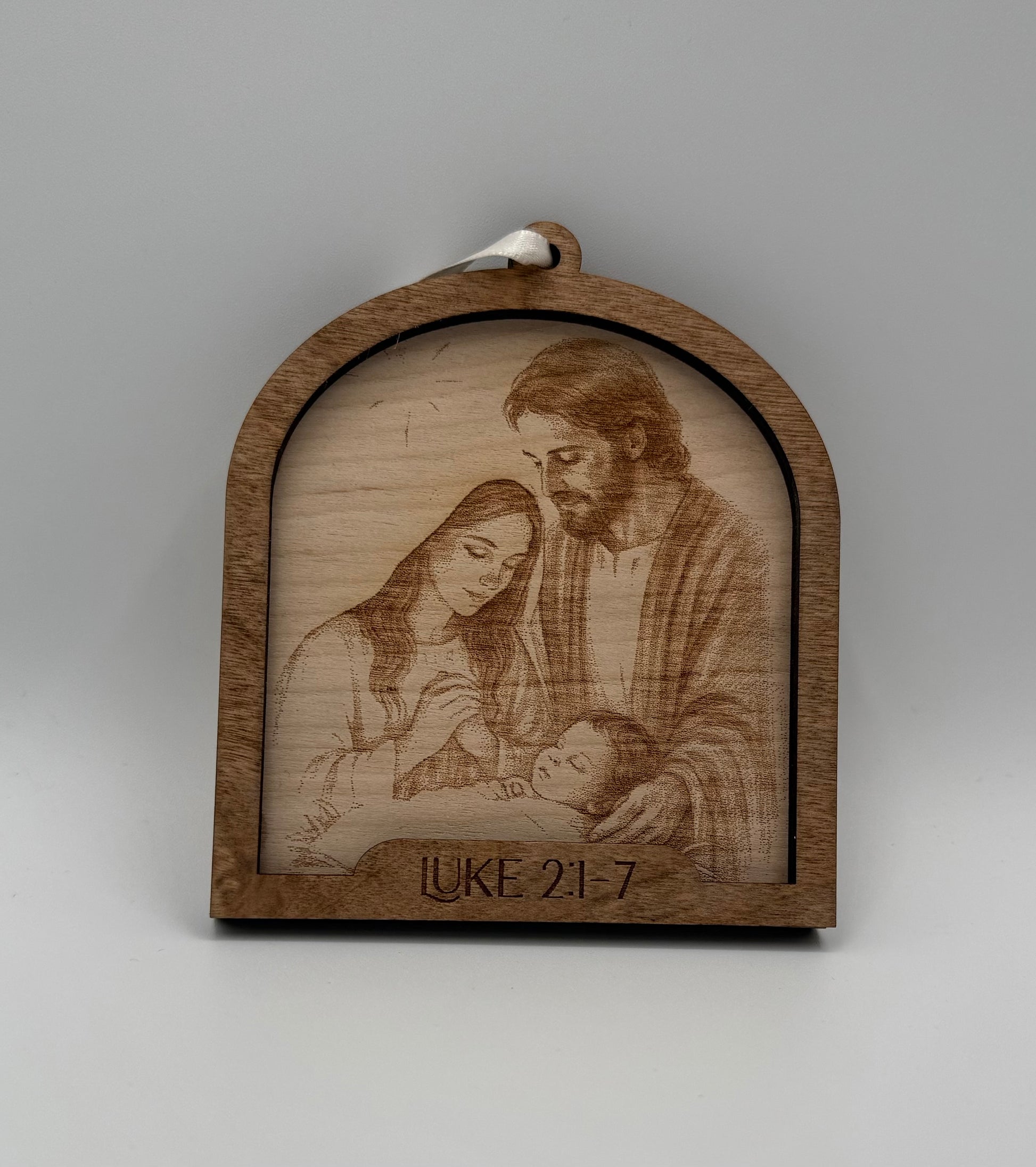 Wooden ornament with a laser engraved scene depicting Mary and Joseph looking at baby Jesus. Bible verses Luke2 2:1-7
