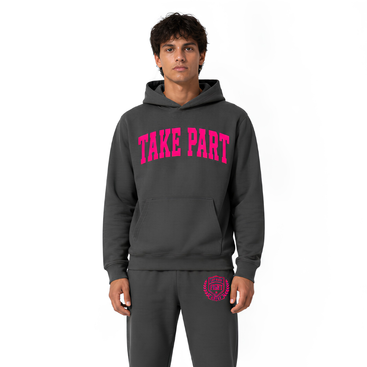 A man modeling a dark gray hoodie and matching sweatpants set. The hoodie features the words 'TAKE PART' printed in bright pink across the chest, and a matching pink circular graphic is printed on the left thigh of the pants.
