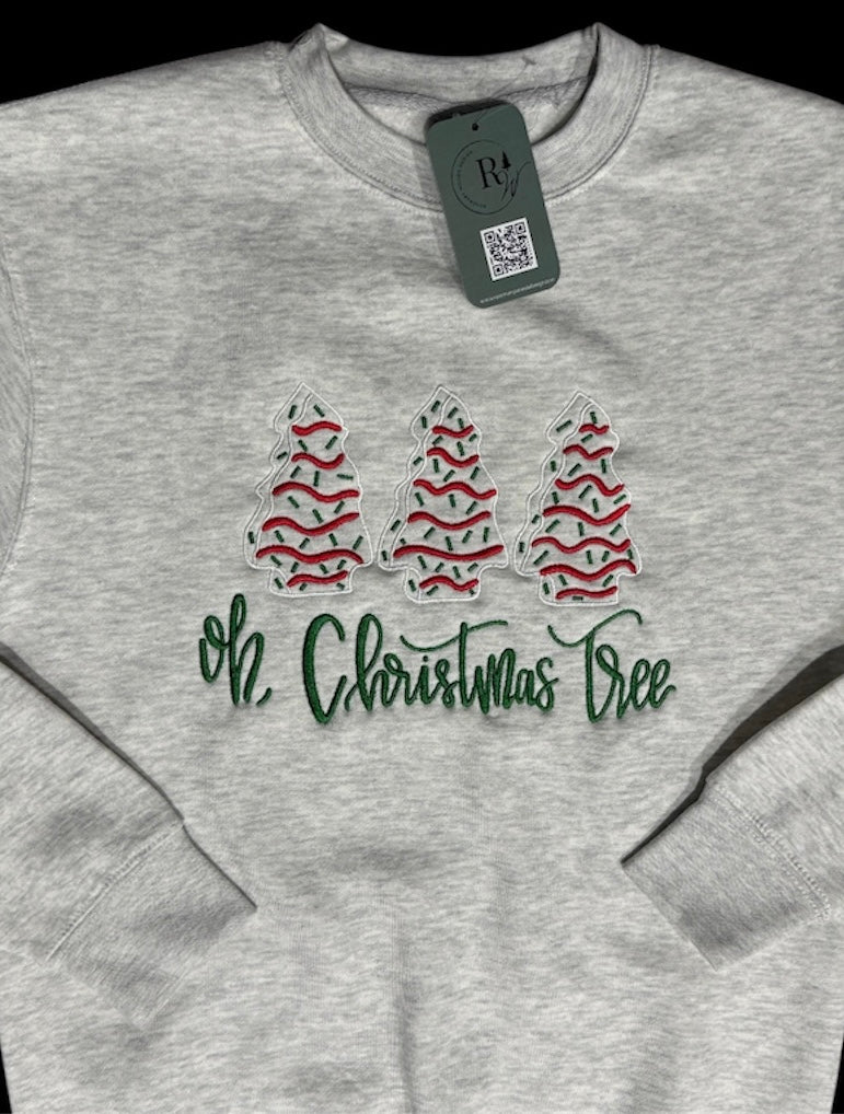 Heathered gray sweatshirt with 3 Christmas trees embroidered in white, red, and green in a line with the text 'Oh, Christmas Tree' embroidered in green underneath. This view is a zoomed in view with sleeves folded on top.
