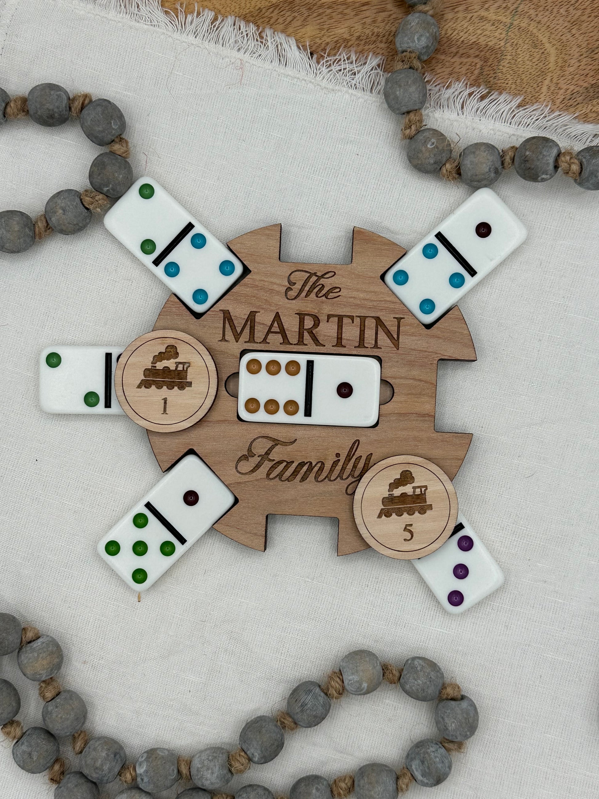 Wooden Mexican train domino center hub with 'The Martin Family' laser engraved on the front on a light background that features wood tokens and dominions for display.