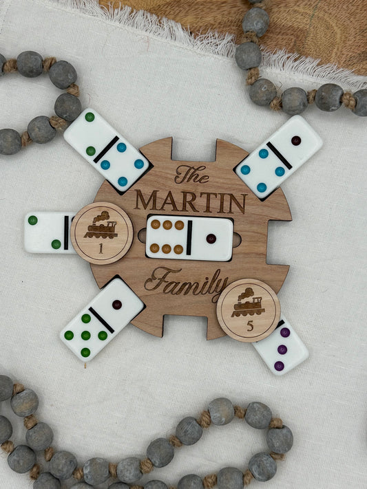 Wooden Mexican train domino center hub with 'The Martin Family' laser engraved on the front on a light background that features wood tokens and dominions for display.