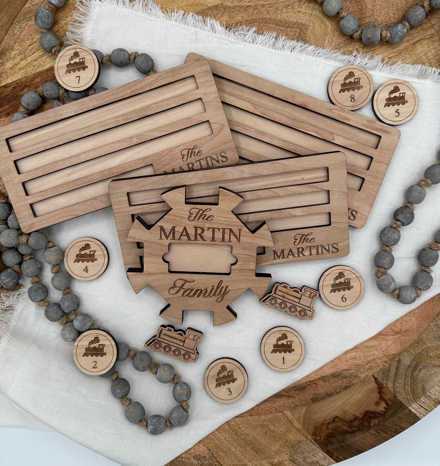 Wooden Mexican train domino center hub with 'The Martin Family' laser engraved on the front and three domino holders with the 'The Martins' laser graved on the front right corner on a light background that features wood tokens and dominions for display.