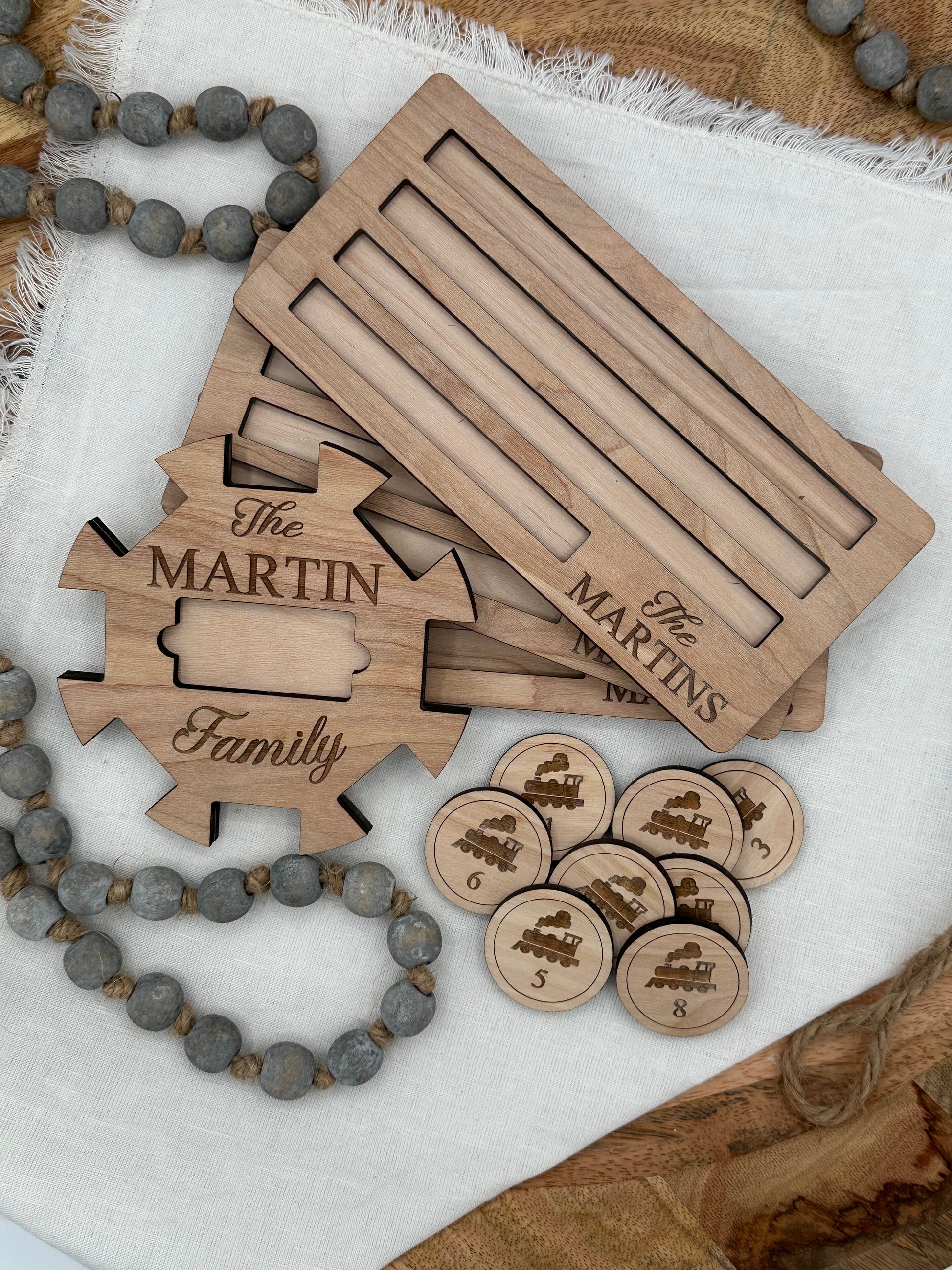 Wooden Mexican train domino center hub with 'The Martin Family' laser engraved on the front and two domino holders with the 'The Martins' laser graved on the front right corner on a light background that features wood tokens with trains on them for display.
