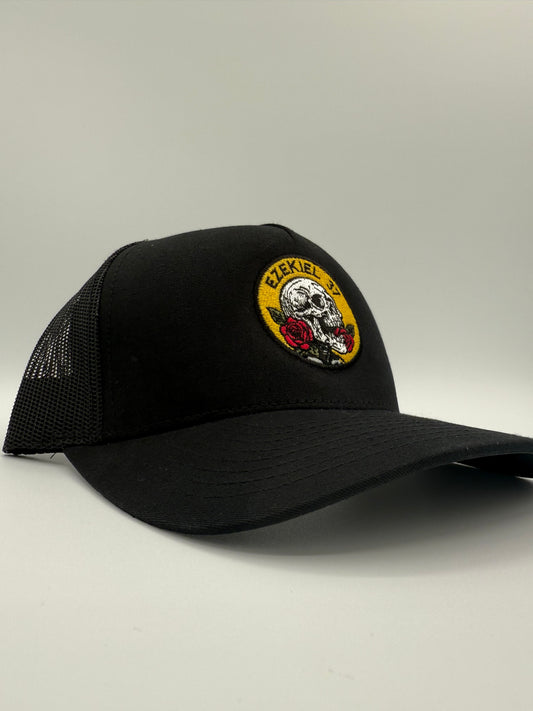 Black hat with a circular embroidered design of a skull with a rose and the words 'Ezekiel 37"